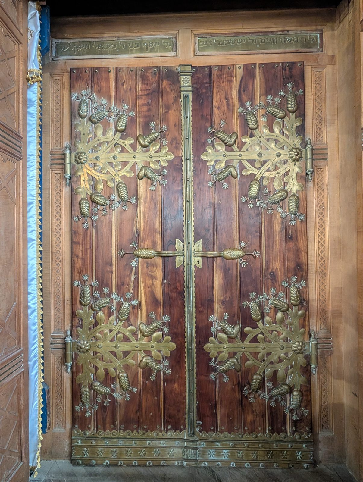 The closed wooden doors of the Torah ark at Szeged, covered with ornate gilded metal fittings in the shape of leaves and flowers, with a Hebrew inscription carved above